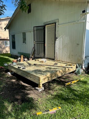 A finished pressure-treated landing decked and level at the back door of a white house, with a level and tools resting on the new boards.